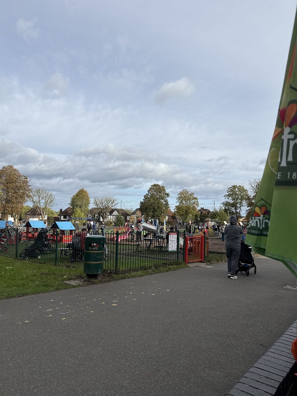 View along the park path to the cafe's outdoor seating area with parasols under a big cloudy sky