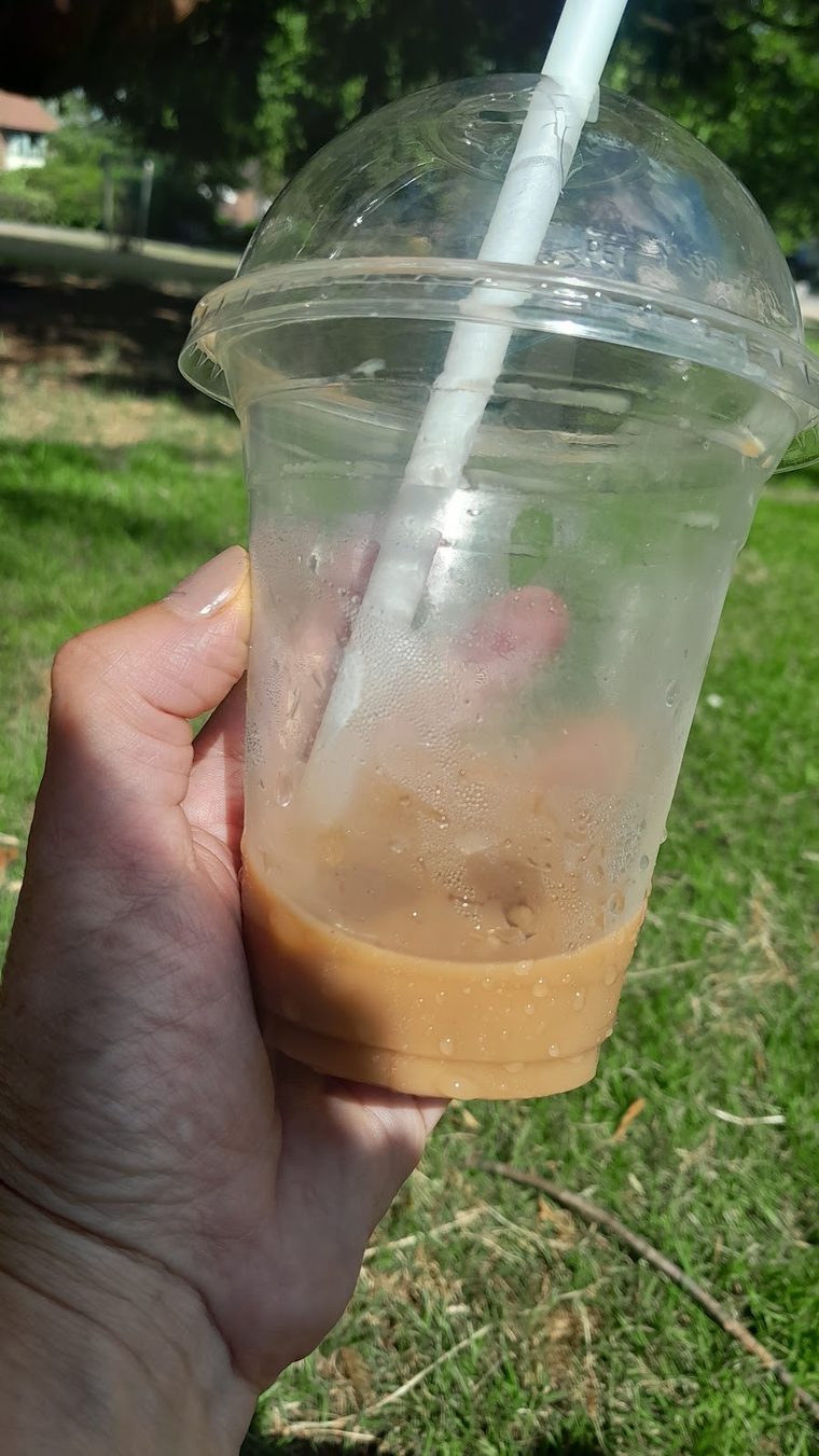 An iced coffee in a clear cup held in the sunlight